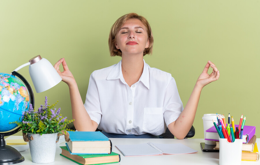 peaceful-young-blonde-student-girl-sitting-desk-with-school-tools-meditating-with-closed-eyes-isolated-olive-green-wall_84b2d.jpg