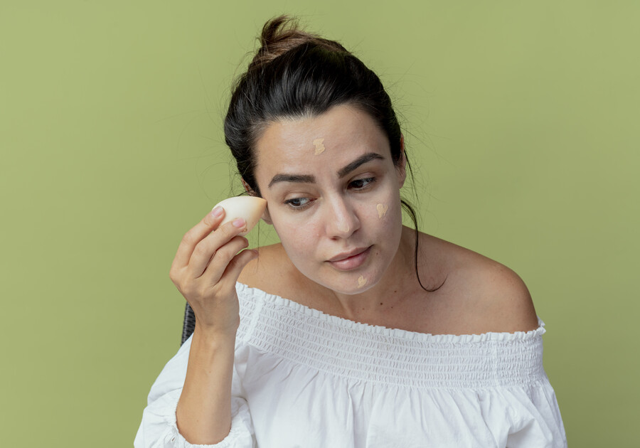 pleased-beautiful-girl-applying-foundation-with-sponge-isolated-green-wall_229f9.jpg