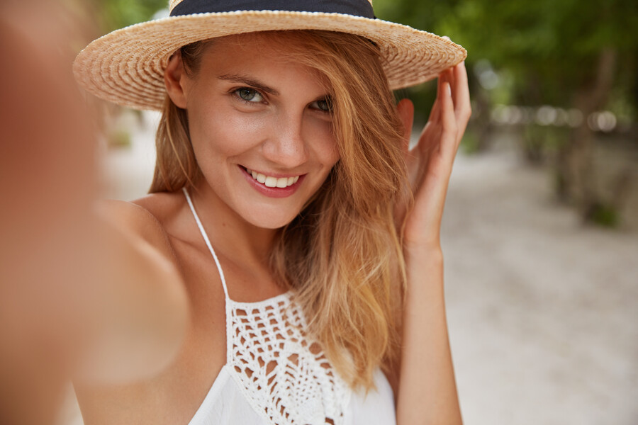 positive-blonde-young-female-with-cheerful-expression-makes-selfie-as-poses-outdoor-tropical-island-wears-fashionable-summer-hat-white-dress_852ce.jpg